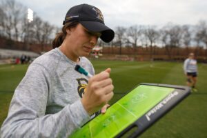 Brenau head coach Emily De Jiacomo makes notes before the first Brenau lacrosse match against Georgetown College on Friday, Feb. 9, 2018 in Gainesville, Ga. (AJ Reynolds/Brenau University)