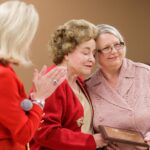 Deborah Bailey, left, applauds as Eva Johnson, right, gets a hug from Sandra Greniewicki as she receives her award during Masters in the Art of Nursing: Healers among us on Thursday, Feb. 15, 2018 at Whalen Auditorium in Brenau East in Featherbone Communiversity in Gainesville. (AJ Reynolds/Brenau University)