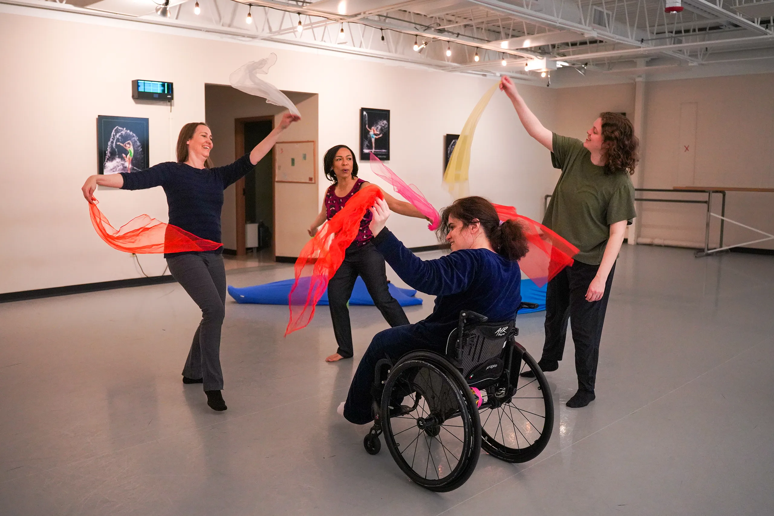 Group of people, some standing, one in wheelchair, doing dance movement therapy with fabric