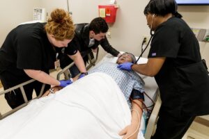 Lauren Bearden tends to a dying patient in the sim lab as theatre students Maggie Todd, center, and Matt Lunsford act as grieving relatives during a death and dying simulation that aims to prepare nurses before they enter a real-life setting. (AJ Reynolds/Brenau University)