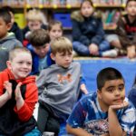 Students sit on a rug and listen to stories.