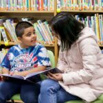 An elementary school student and college student read to each other. 2