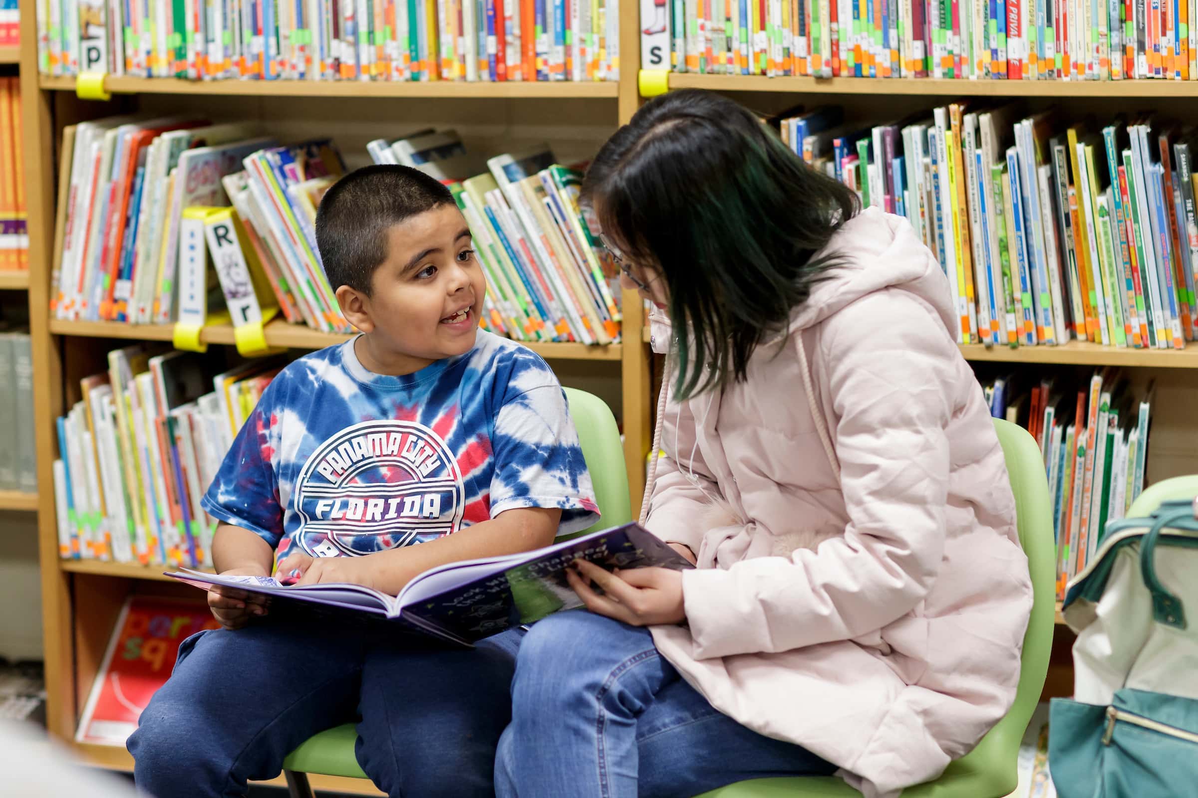 An elementary school student and college student read to each other. 2