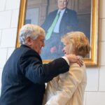 Two people talk in front of a painting.