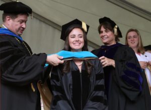 Brenau University Provost James Eck, left, and Chair of the Physical Therapy Department Kathye Light fixes the academic regalia of Sarah Gay as she receives her doctorate in physical therapy during the graduate and undergraduate commencement Saturday May 5, 2018 in Gainesville, Ga. (Jason Getz for Brenau University)