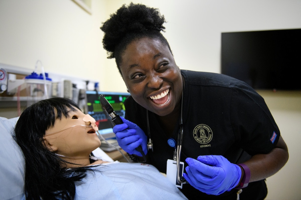 A nursing student laughs while preparing to work with a medical manikin.