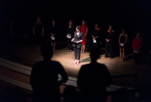 Two audience members stand as “The Vagina Monologues” cast member Ginny Early asks any victims of violence to stand in solidarity as she reads a monologue about sexual violence during the performance in Gainesville on Aug. 10, 2019, at Pearce Auditorium on the historic Gainesville campus. (Nick Bowman for Brenau University)