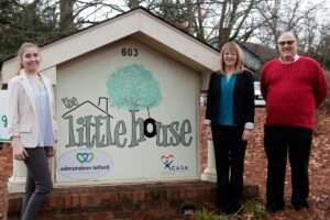 Three people stand by a sign for the Little House in Gainesville