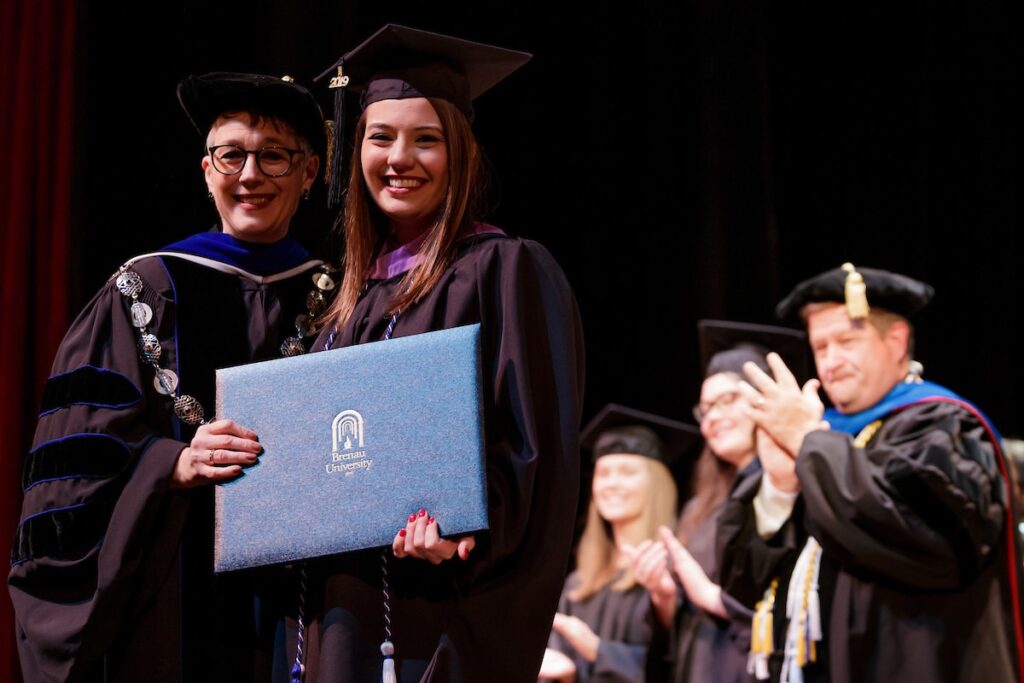 student posing with the president as she hands her diploma