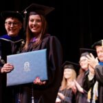 student posing with the president as she hands her diploma