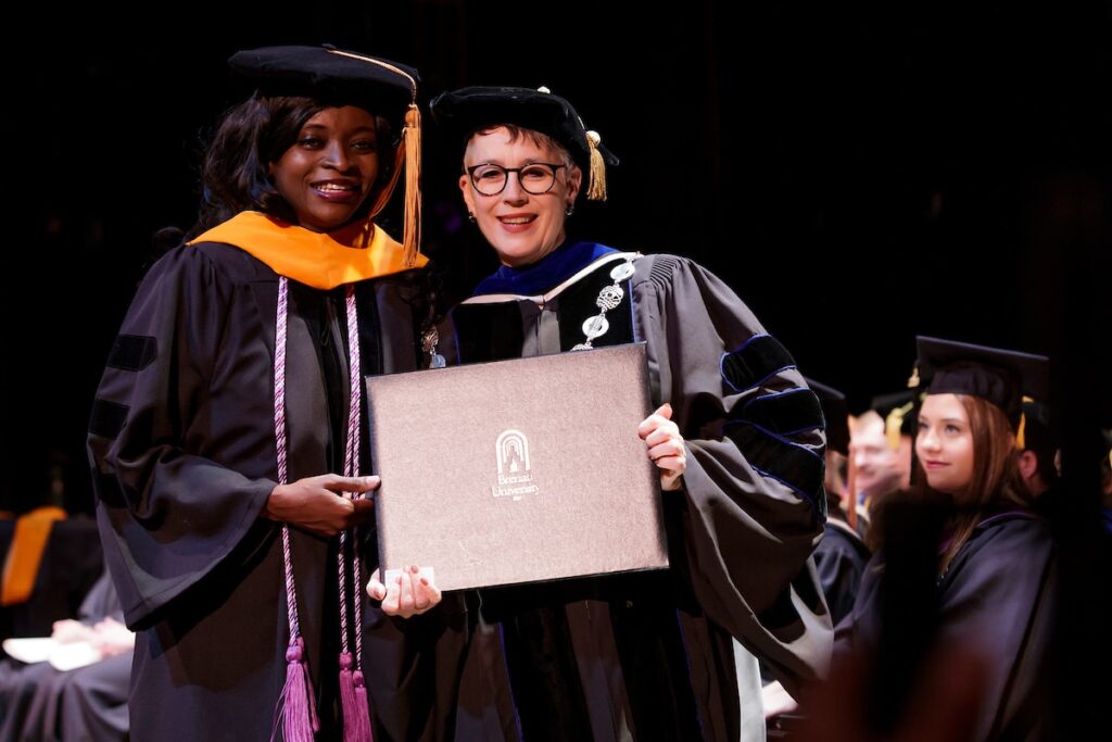 president posing with student as she receives her diploma