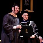 student with the president as he receives diploma