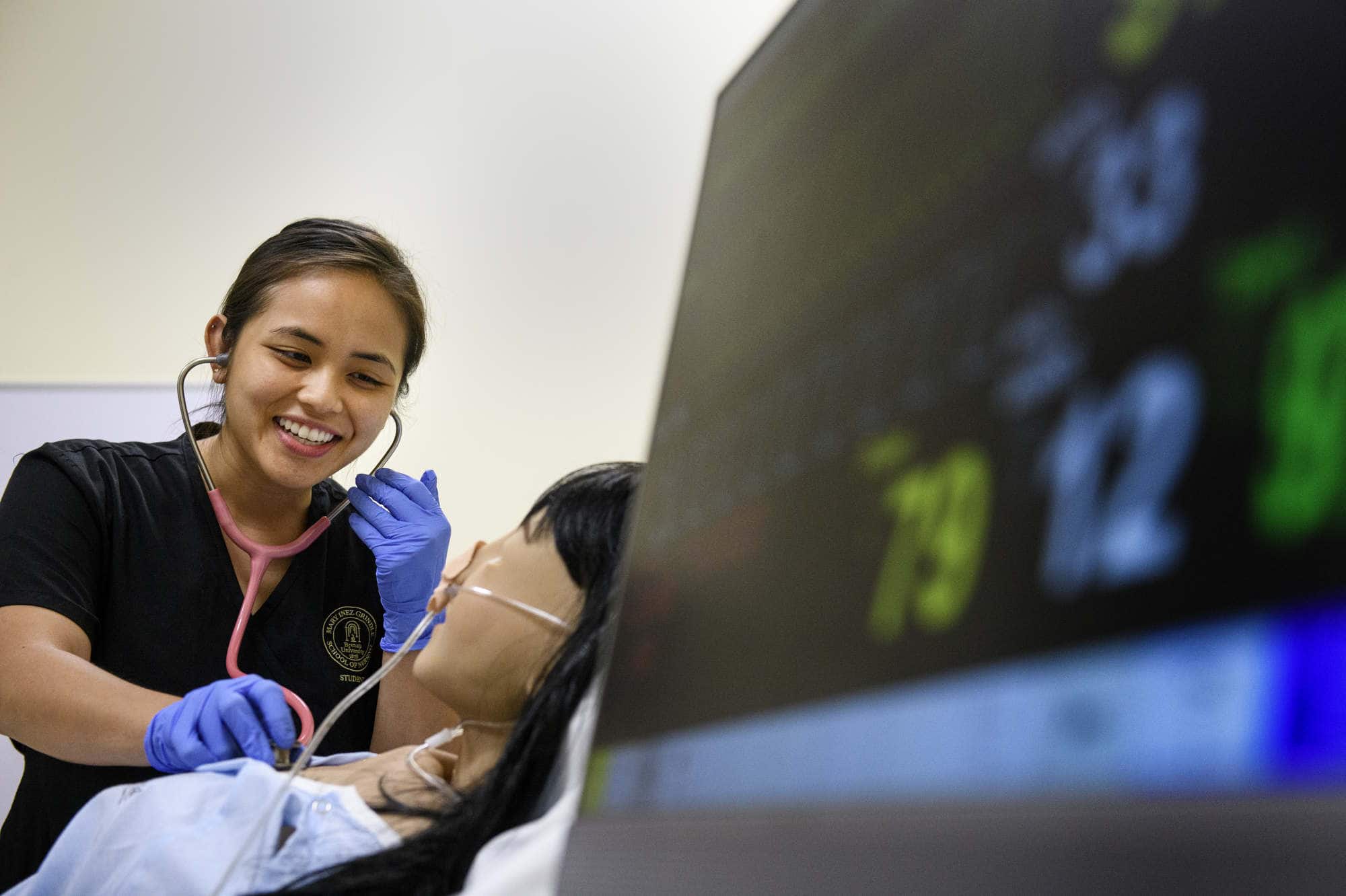 A nursing student works on a simulator with a monitor in the foreground