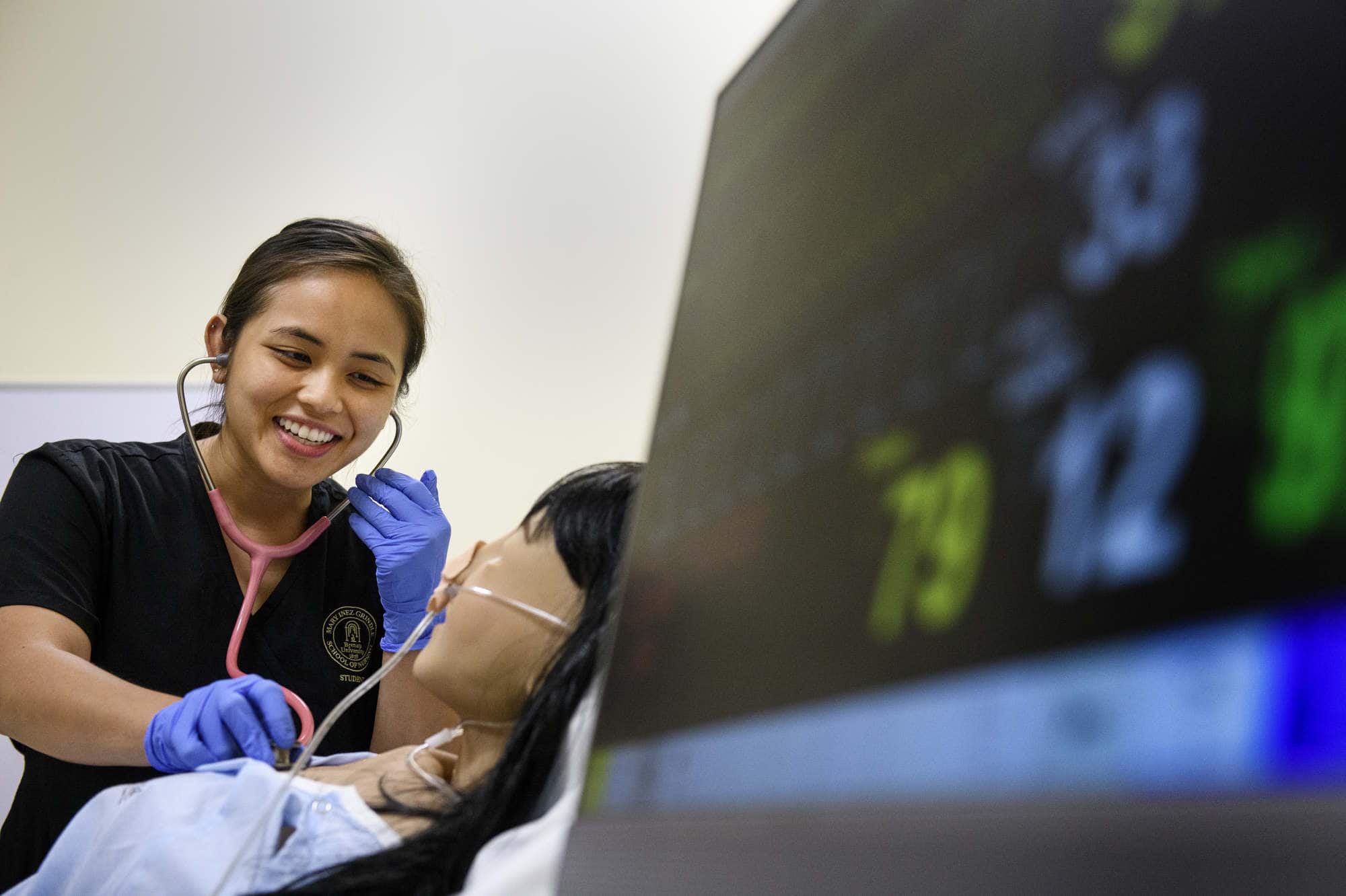 A nursing student works on a simulator with a monitor in the foreground