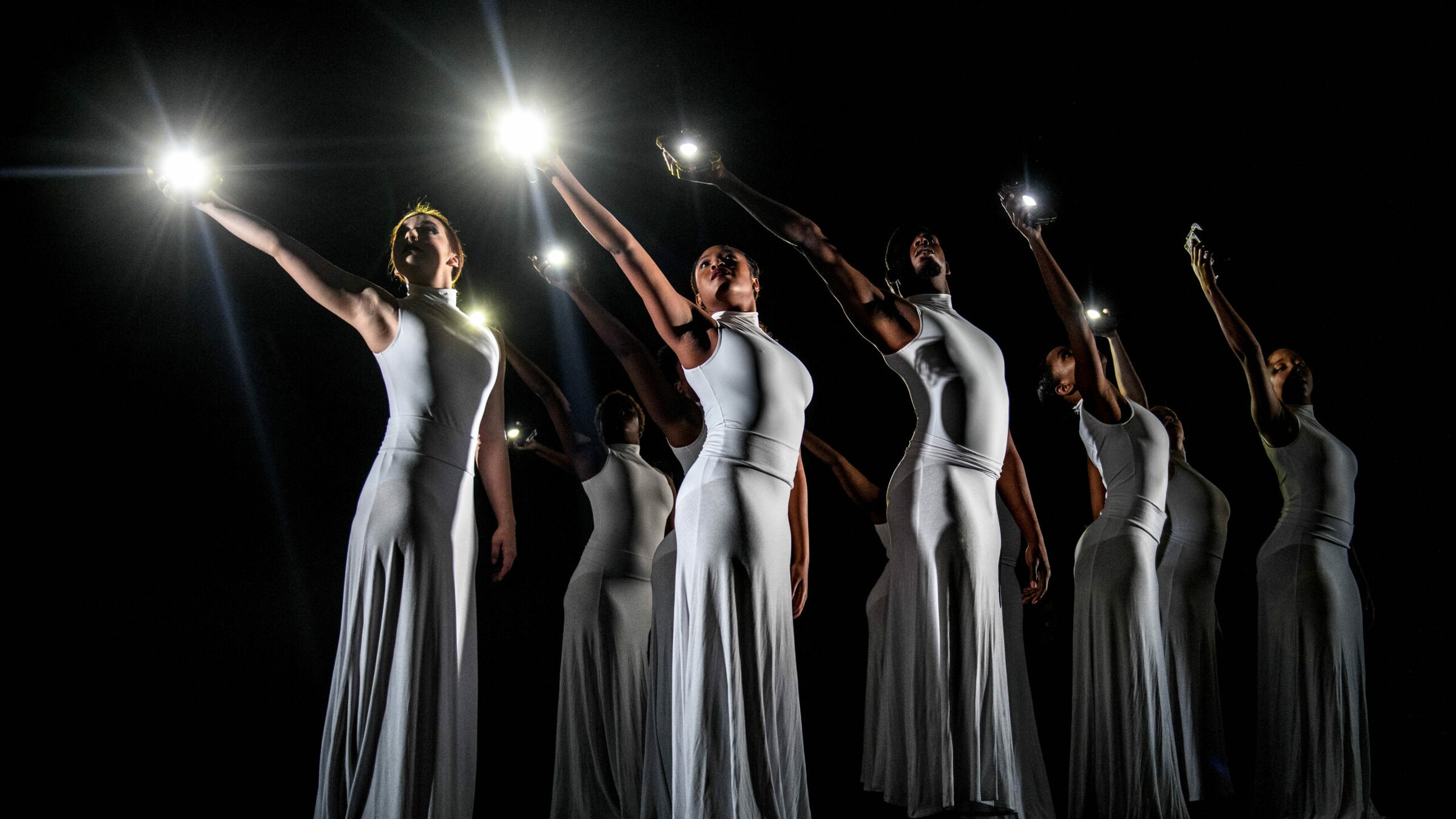 A group of dancers hold lights in the air while performing on stage