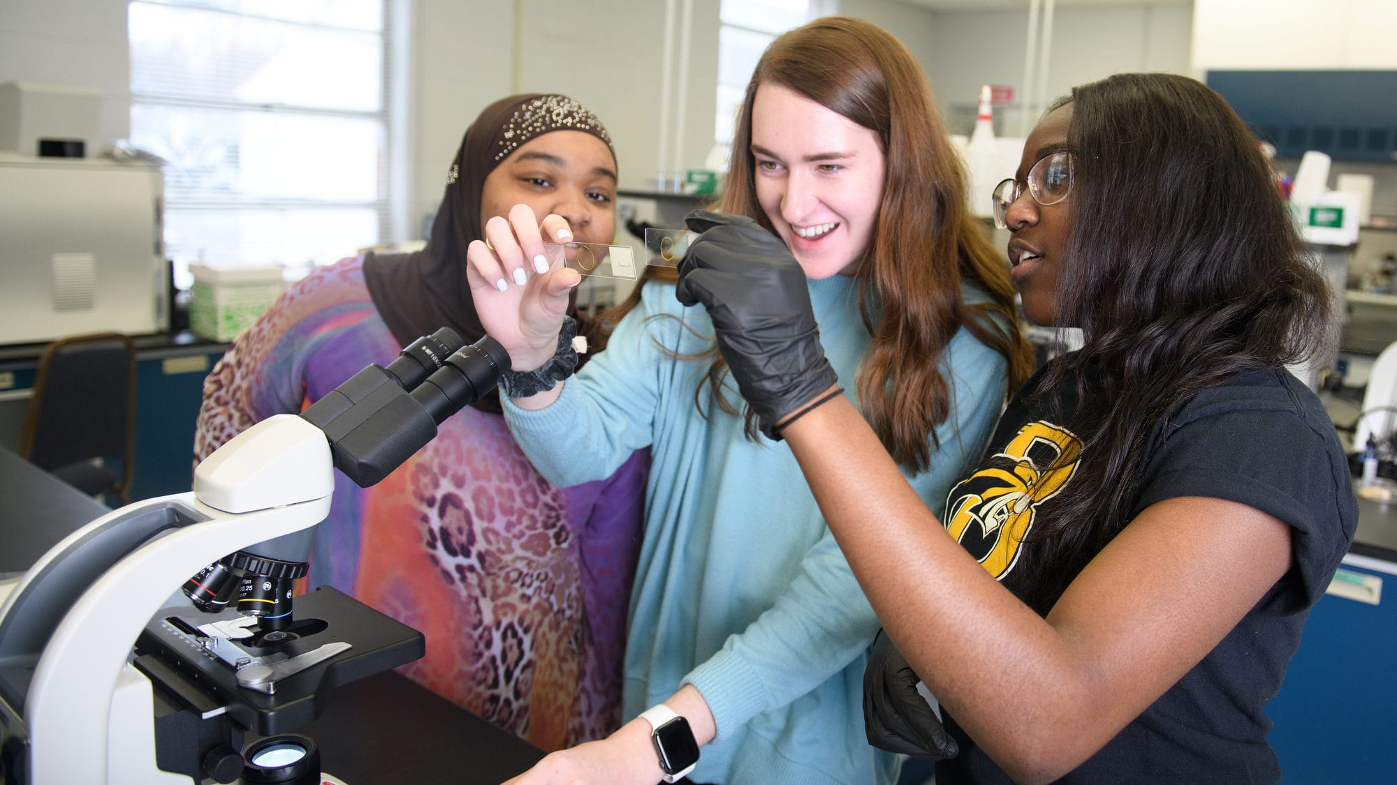 Three students examine microscope slides in a biology lab
