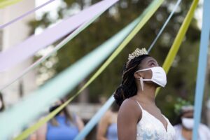 Colorful streamers and a woman wearing a crown and face mask at Brenau University outdoor event.