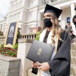 Woman in regalia carries diploma cover