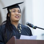 Ms. Joy Nzurike gives invocation at a podium