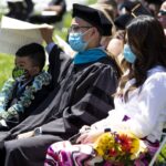 family of three, center figure in regalia, watches ceremony