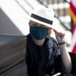 staff member Lainey Kennedy in fedora seated by diploma covers