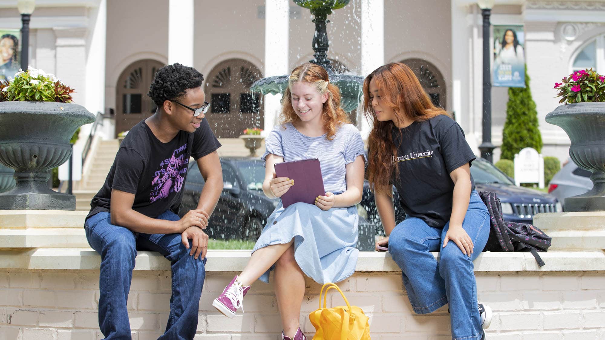 Students sitting at the fountain, looking at an ipad