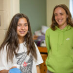 Two roommates pose for a photo outside their dorm room.