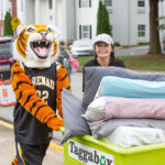 HJ the tiger and a volleyball player help move a student's belongings in a cart