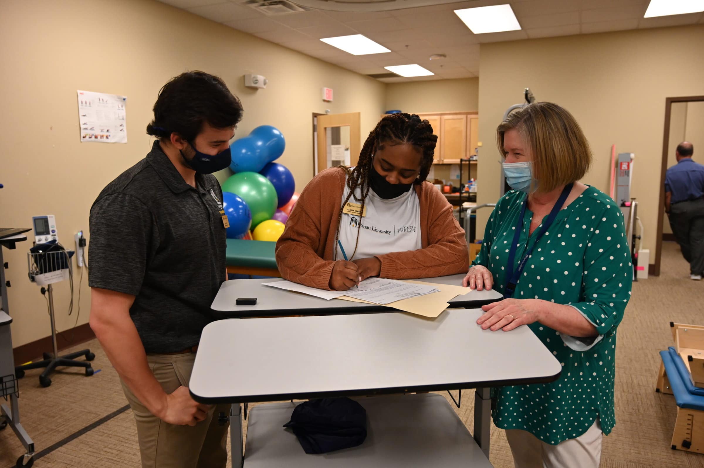 Two physical therapy students work with liaison Dr. Mary Thigpen on paperwork.
