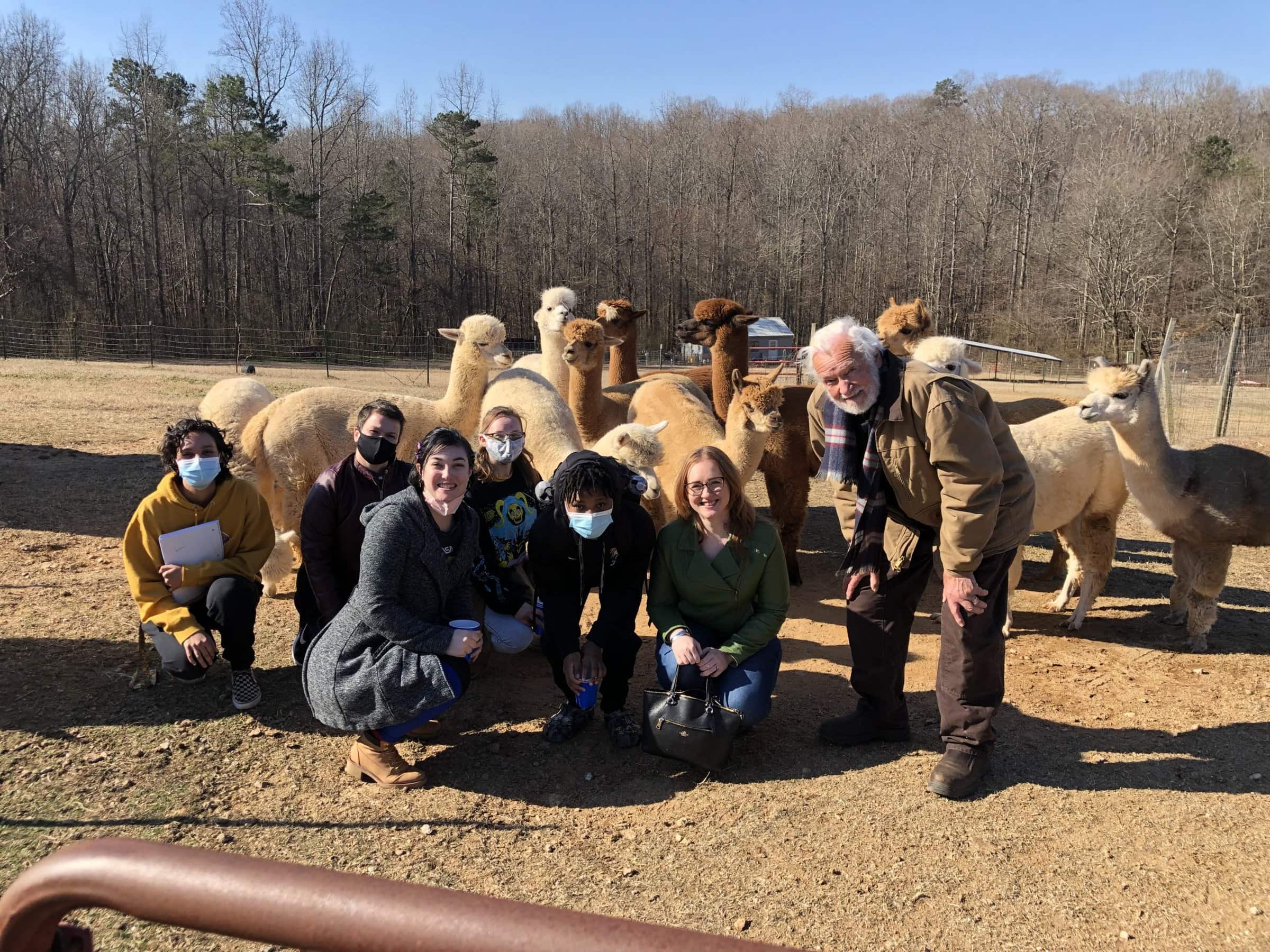 Textile class posing in front of alpacas