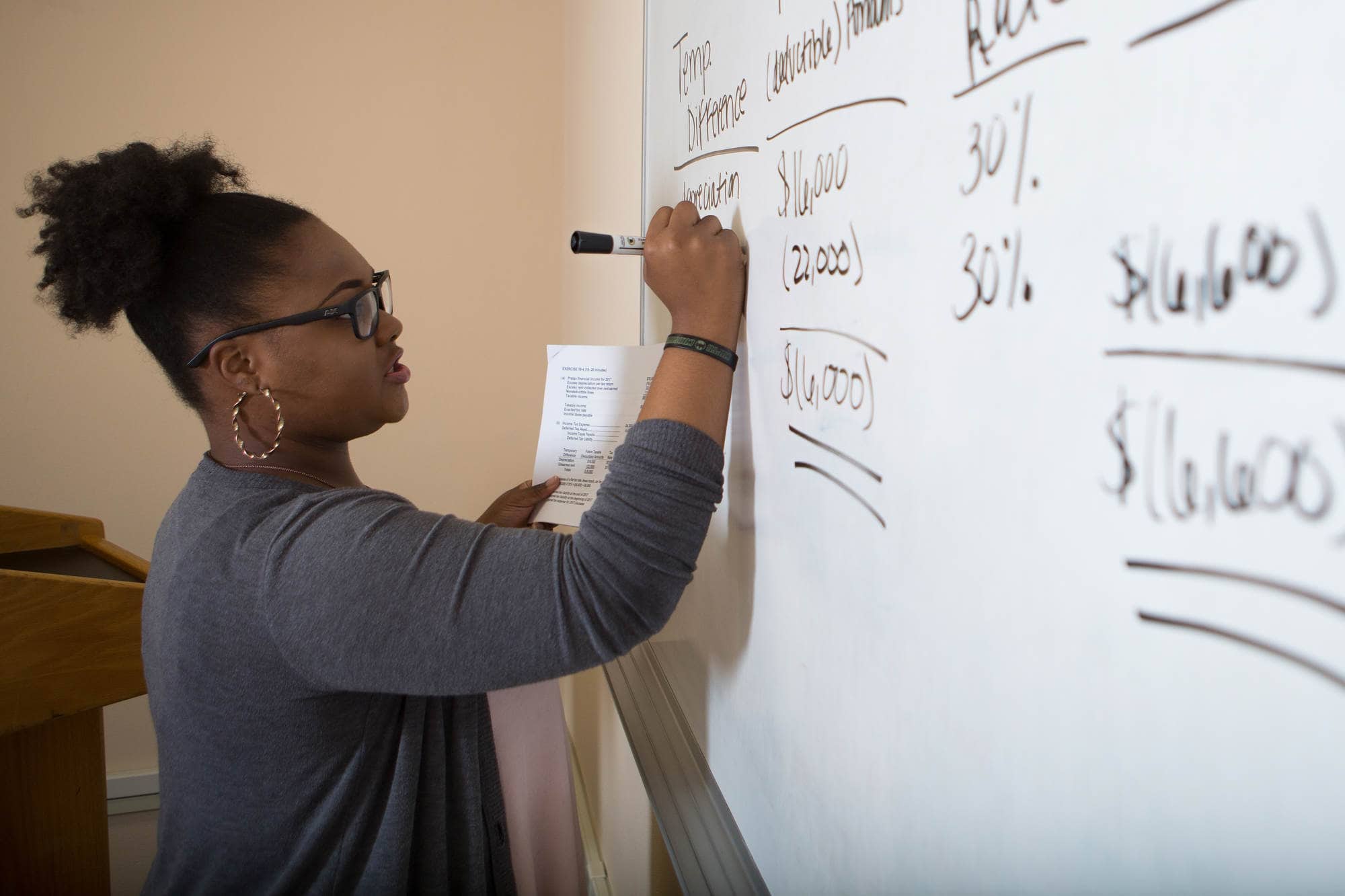 A student works out an accounting problem on a whiteboard