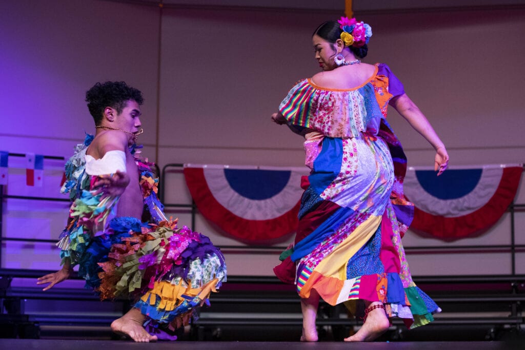 A male and female Panamanian student dance a traditional dance in colorful costumes.