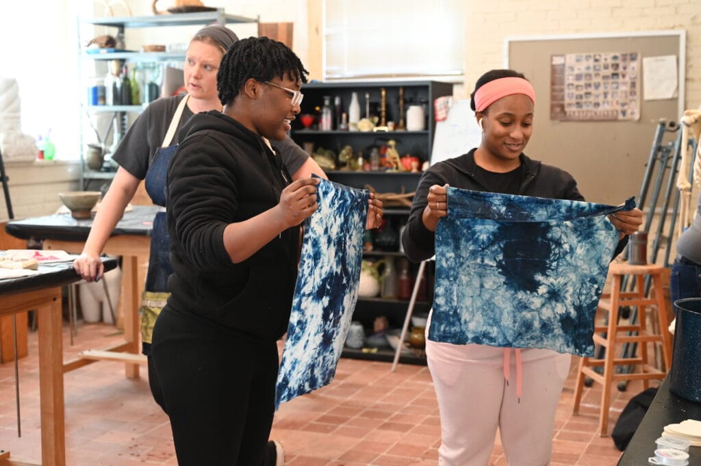 Two students hold up their finished cloths, dyed using indigo.