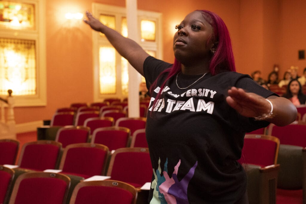 student in black t-shirt stands with arms outstretched