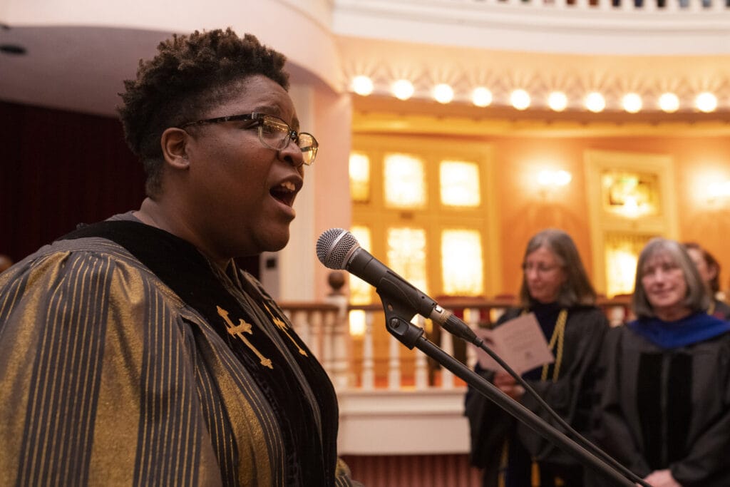 woman in robes sings into a microphone