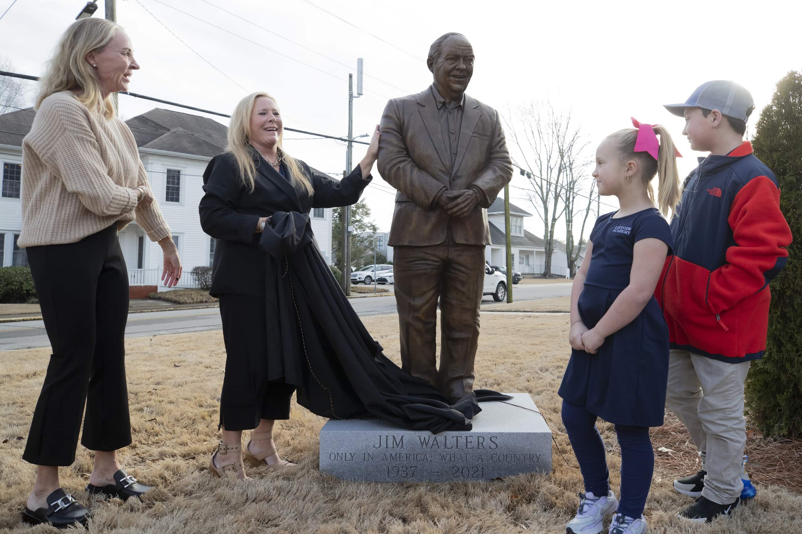 two adults and two children stand on either side of a bronze statue