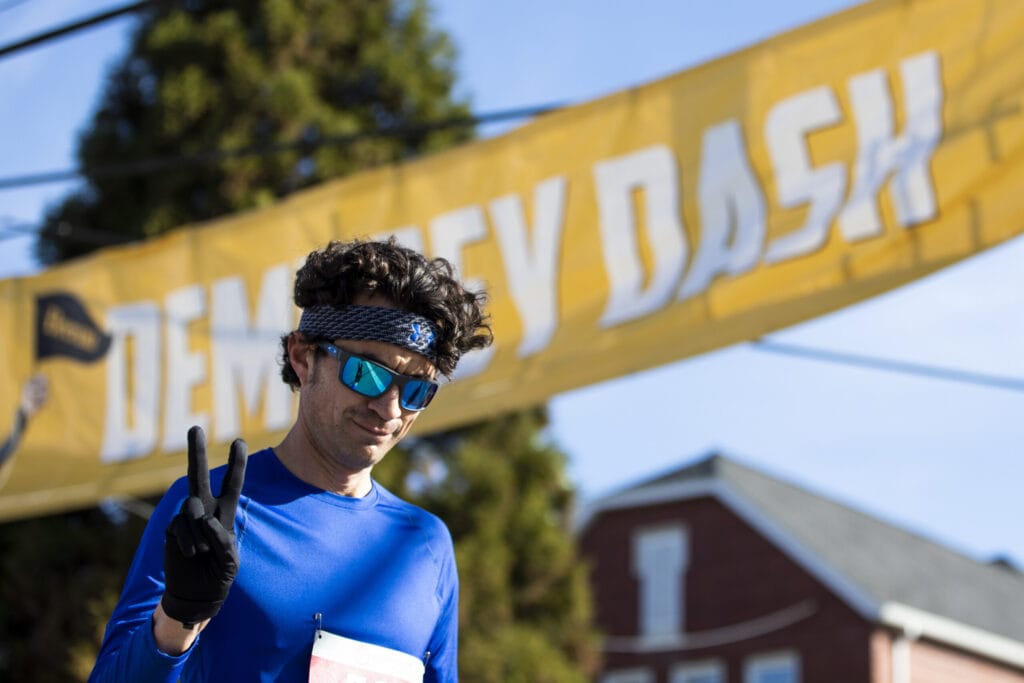 A male runner makes a peace sign in front of the Dempsey Dash banner.