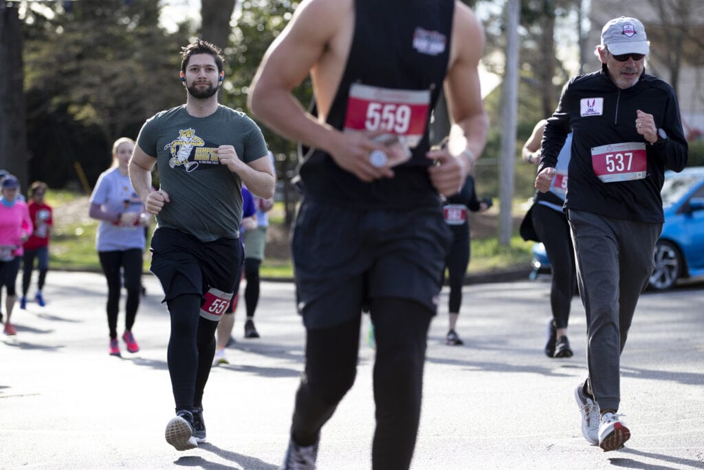 A male runner in a Dempsey Dash t-shirt is framed between other runners.