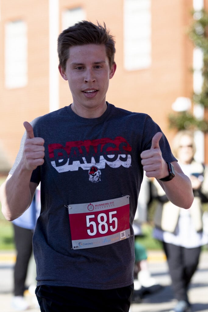 A male runner gives two thumbs up as he runs the Dempsey Dash course