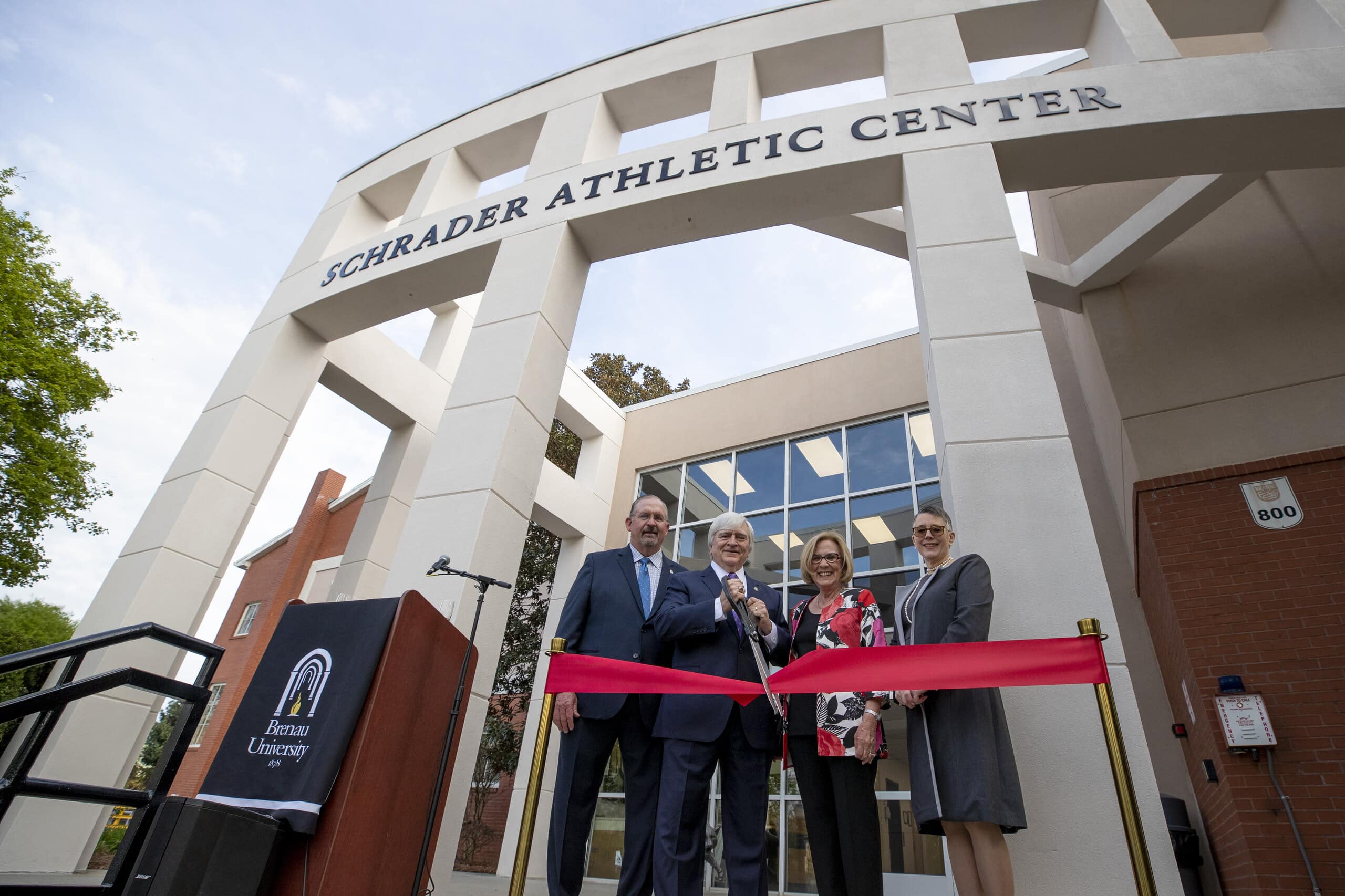 Four people stand with red ribbon in front of building for Schrader Athletic Center event