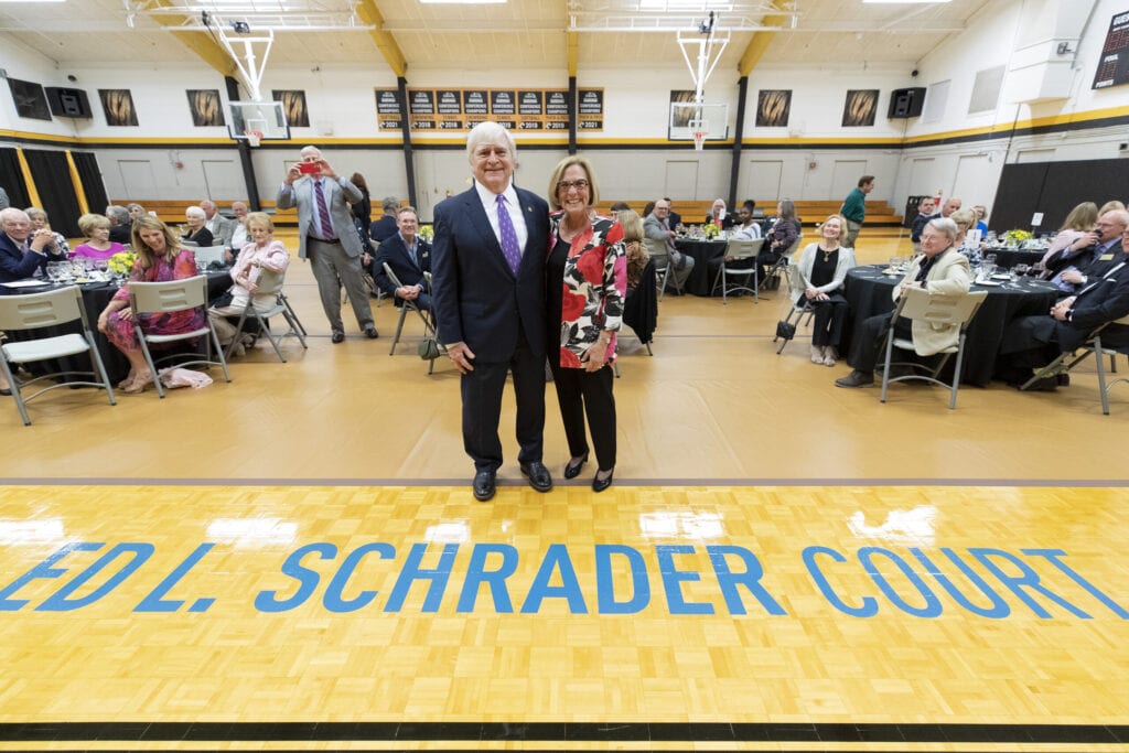 Man and woman stand on basketball courts at letters reading "Ed L. Schrader Court"