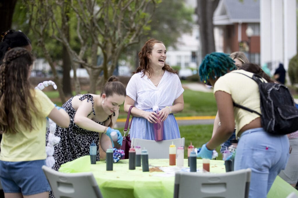 Four students laugh as they tie-dye t-shirts during field day.