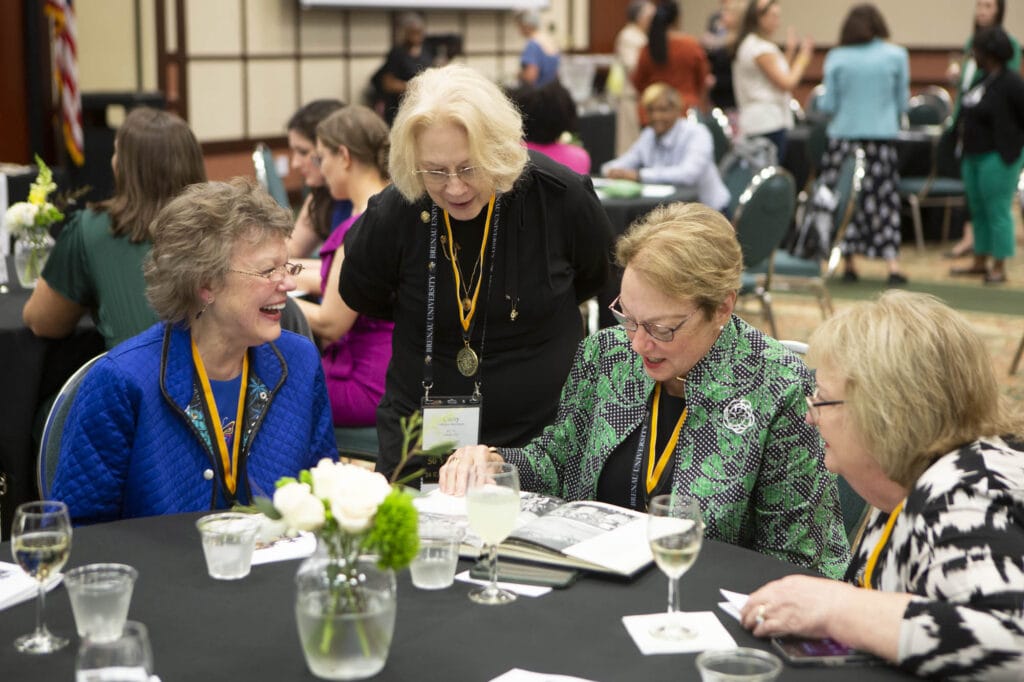 group of alumni sit at a table laughing and looking at yearbook