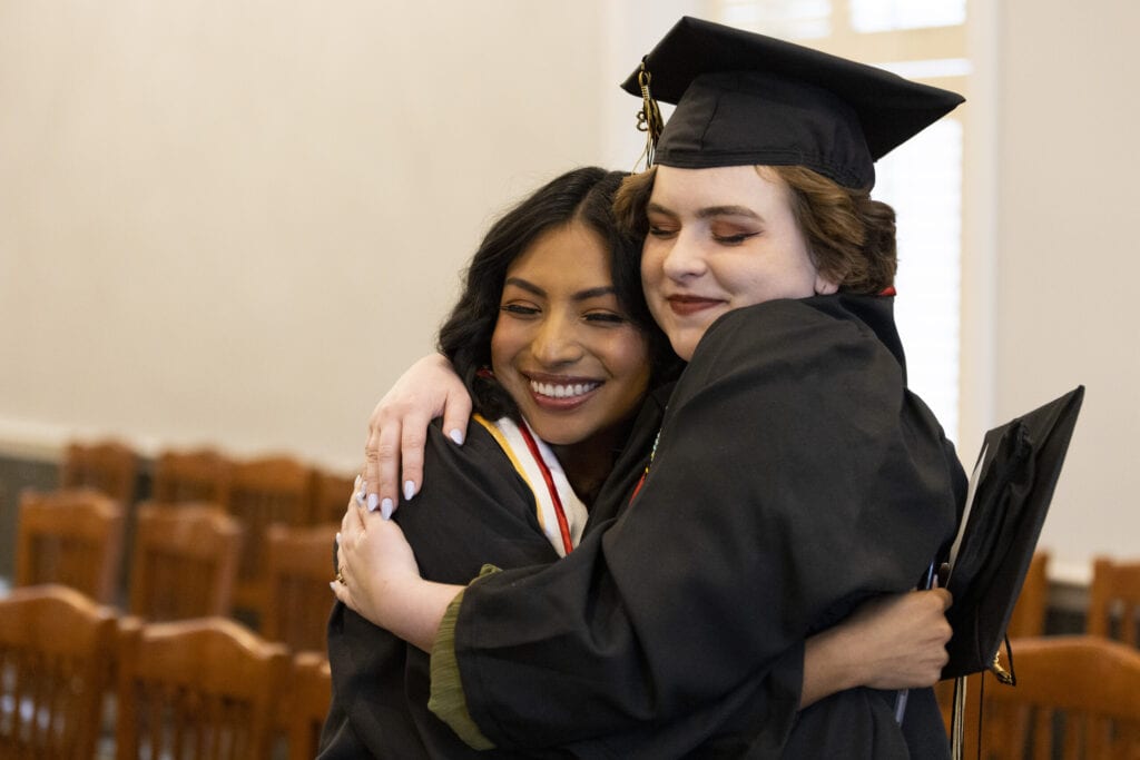 Two Women's College graduates embrace before they process in to the ceremony on Friday.