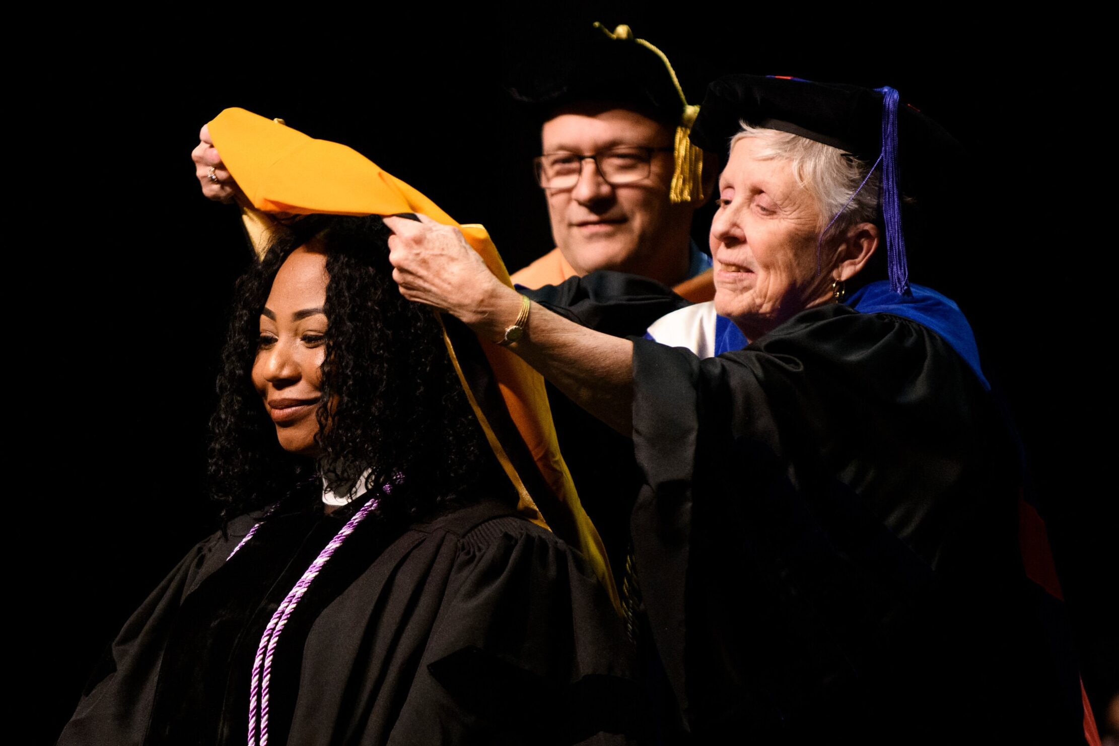 Jill Hayes places a hood on a student's shoulders during a hooding ceremony.