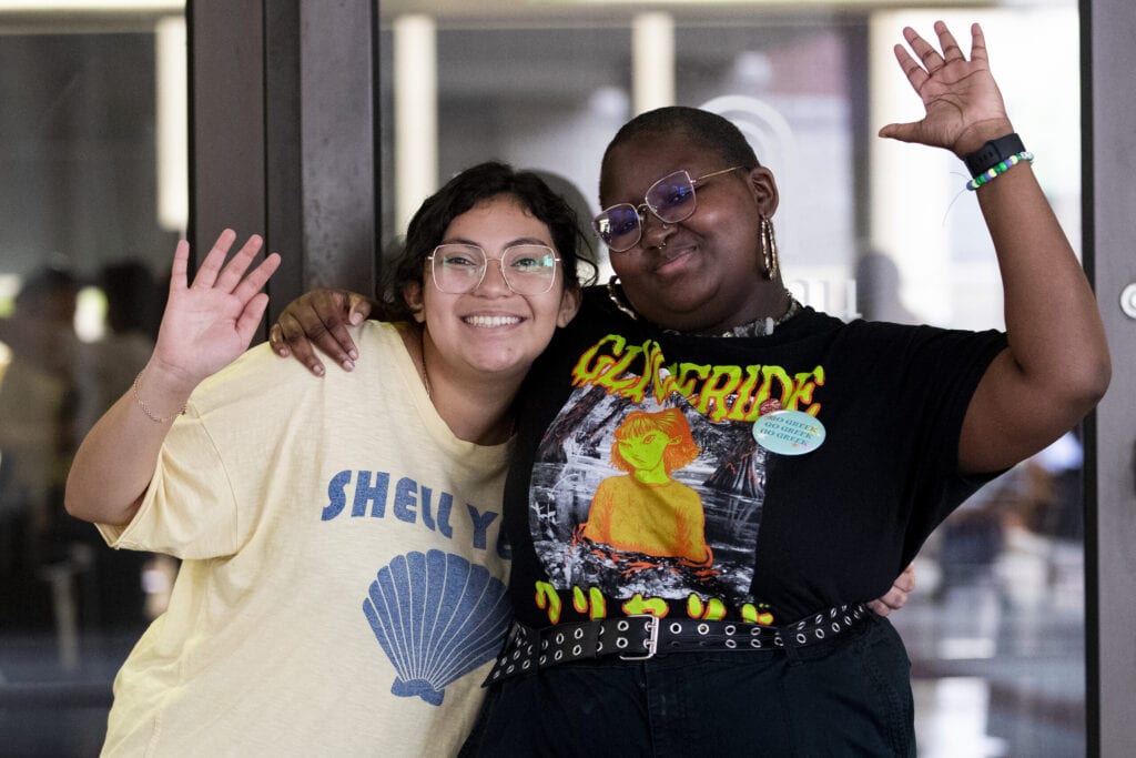 Two female students wave at the camera.