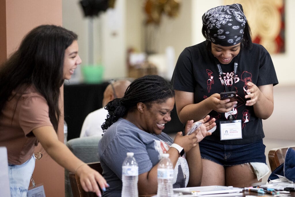 Three female students laugh while sharing something on their phones