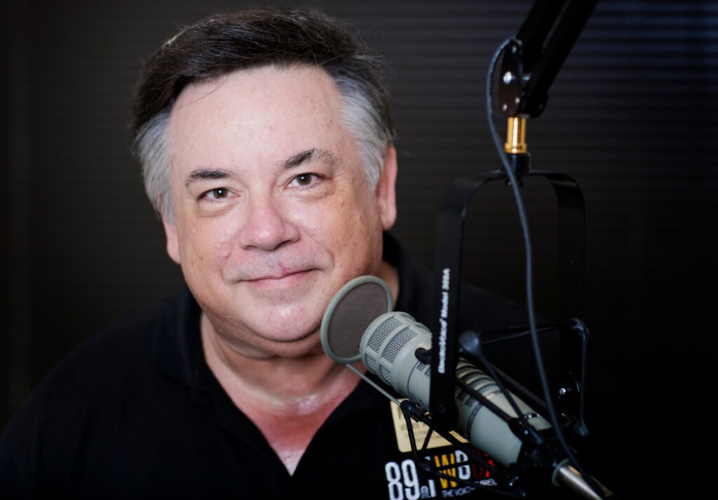 A portrait photo of Jay Andrews with a microphone.