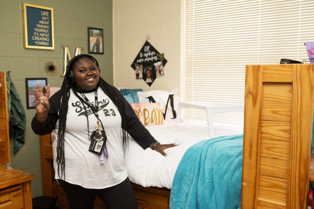 A new student poses next to her decorated side of the room.