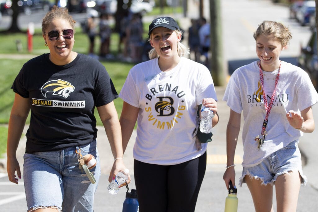 Two swim team members smile while walking alongside a new student.